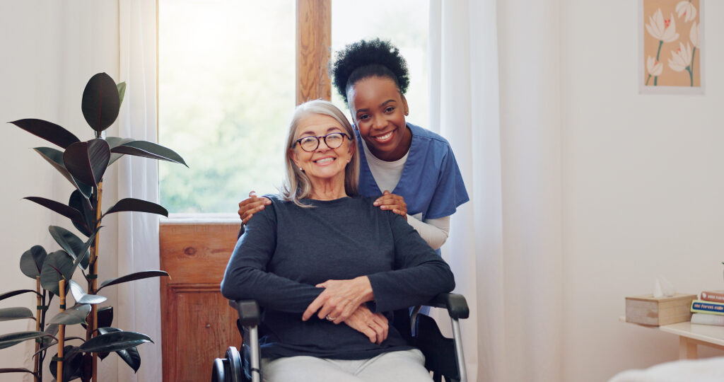 Caregiver smiling with a senior woman seated in a wheelchair at home