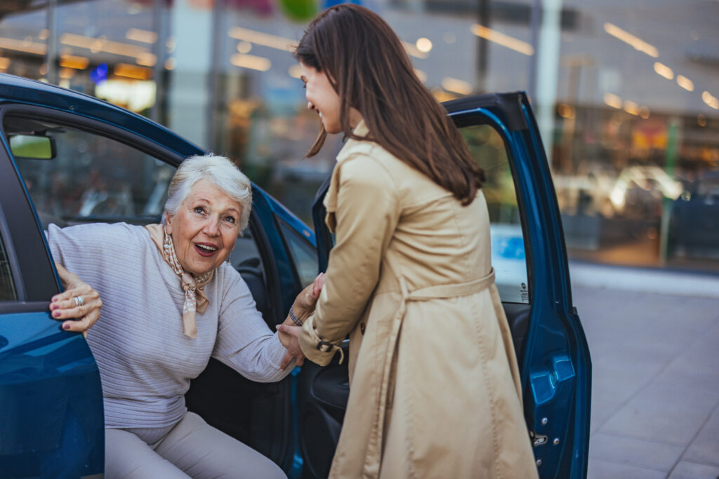 Caregiver helping a senior woman step out of a car in the evening